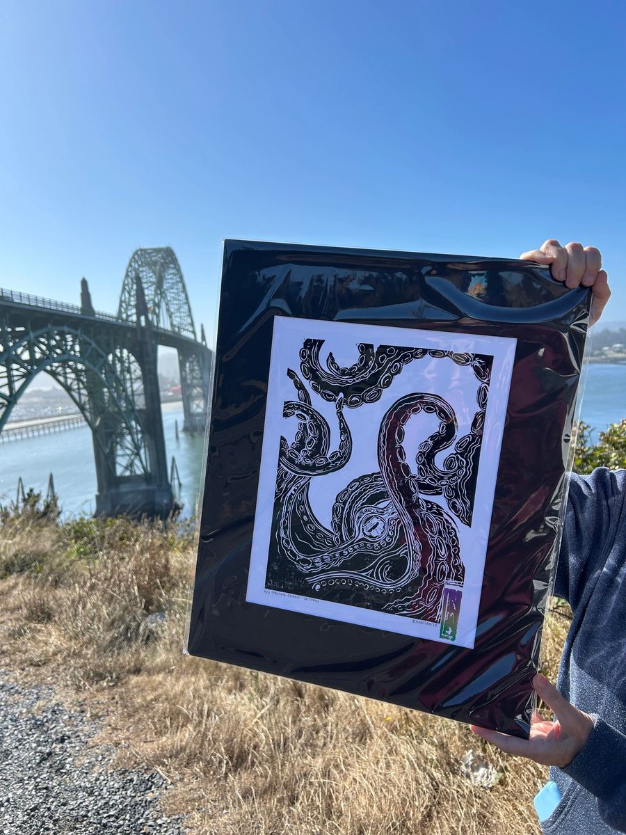 A framed octopus block print held up in front of the Yaquina Bay Bridge